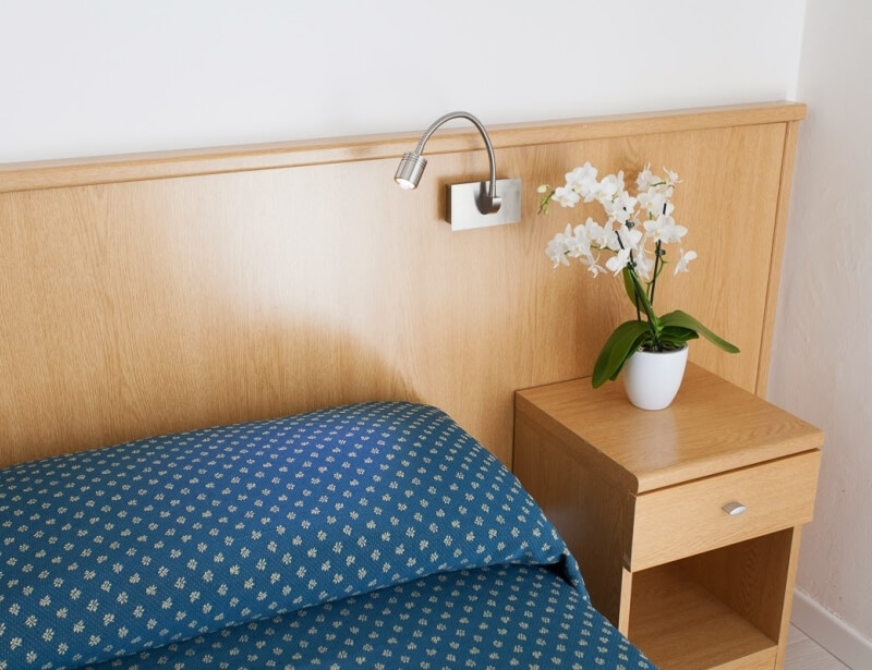 Camera d'hotel con letto, comodino e orchidea in vaso.