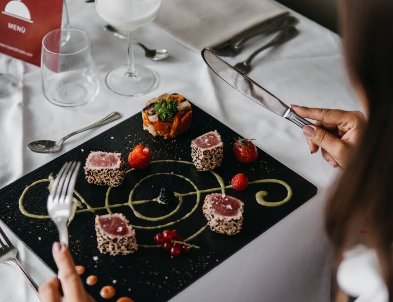 Cubetti di tonno con sesamo, fragole e verdure su piatto nero.
