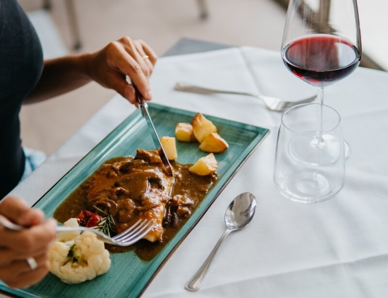 Persona che mangia un pasto con carne, verdure e vino rosso.