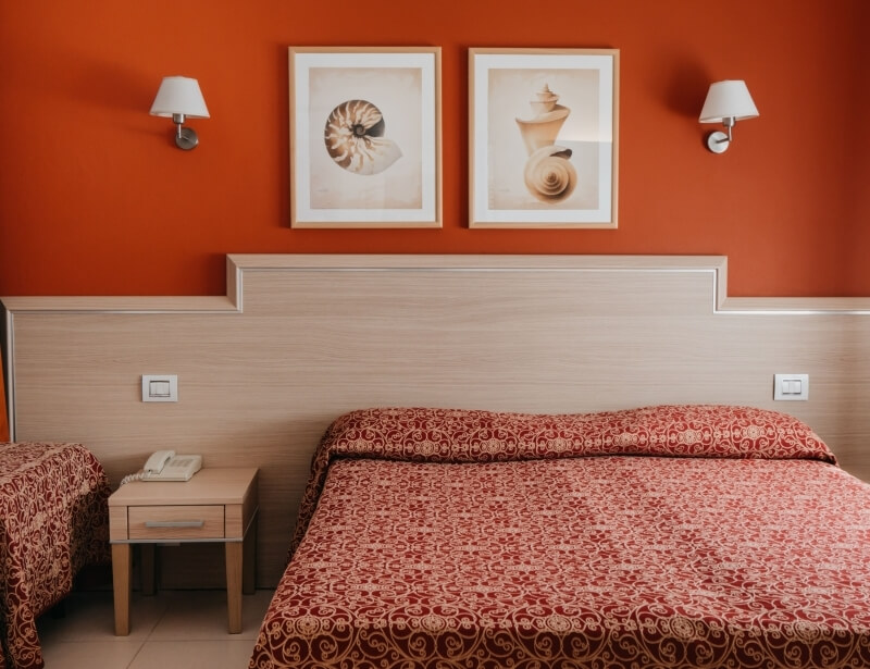 Camera d'hotel con due letti, pareti arancioni e decorazioni marine.