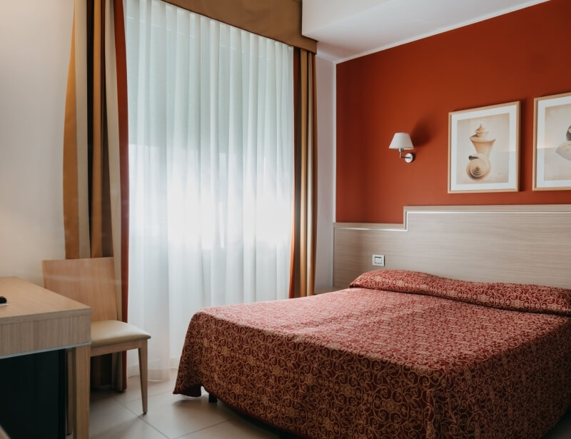 Camera d'hotel con letto, scrivania e finestre con tende a righe.