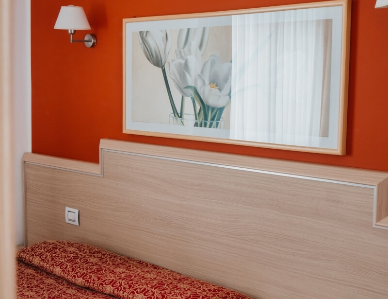 Quadro di tulipani bianchi su parete arancione sopra un letto.