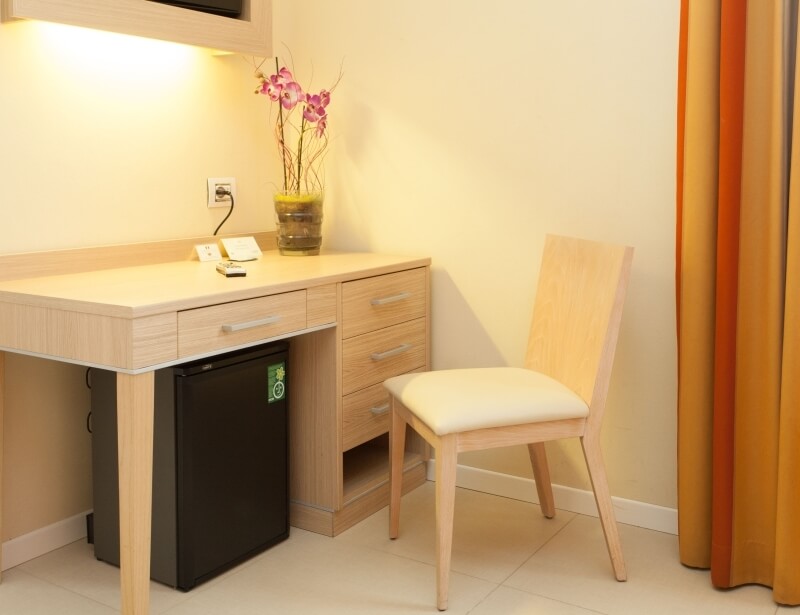 Camera d'hotel con scrivania, frigorifero e sedia in legno.