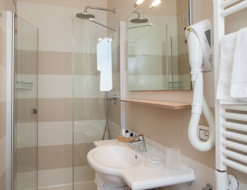 Bagno d'hotel con lavabo, doccia, specchio e asciugamani bianchi.