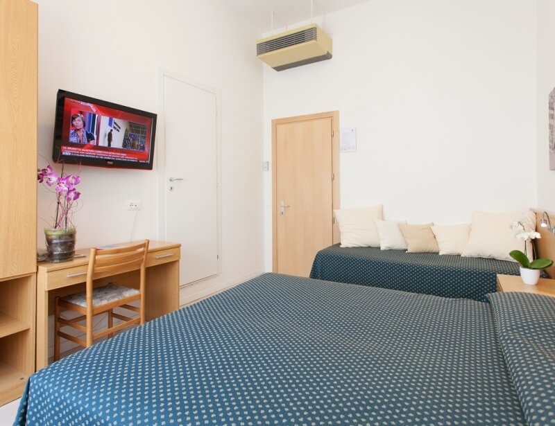 Camera d'hotel con due letti, divano, scrivania e TV.