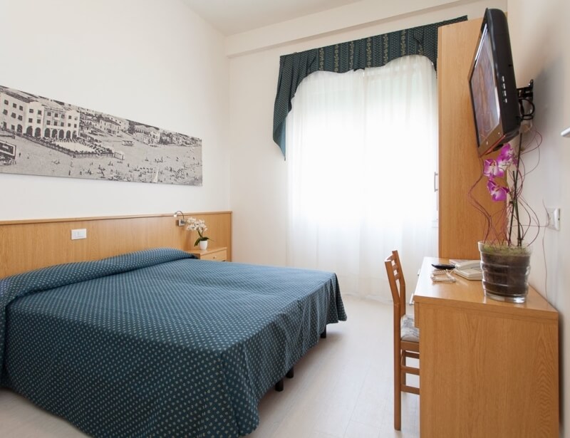 Camera con letto, armadio, scrivania e finestra con tende.