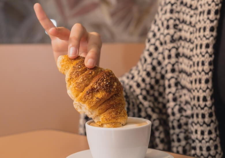 someone dipping their croissant in coffee 