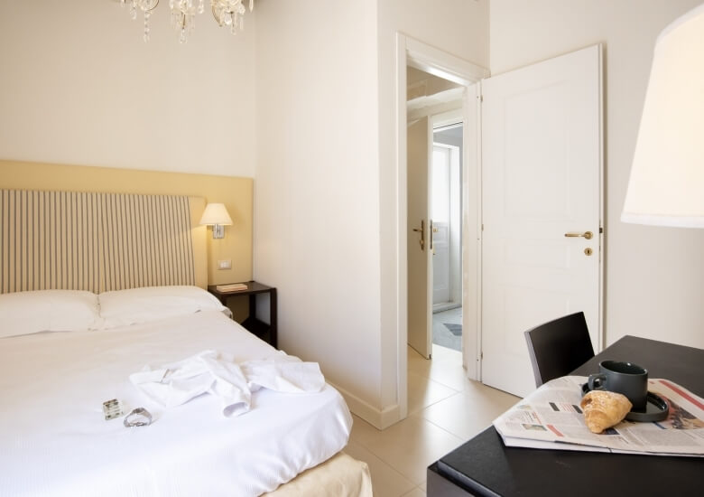 room with clock on the bed and croissant and coffee on the table 