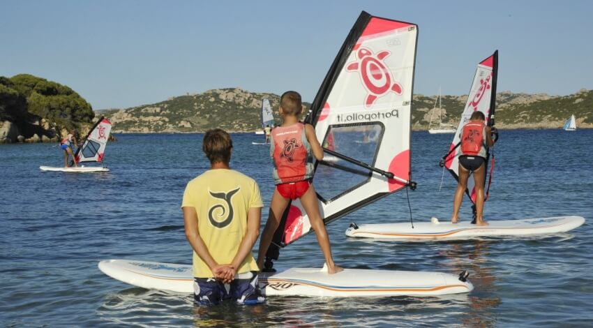 Gruppo di persone windsurfing su un corpo d'acqua con colline sullo sfondo.
