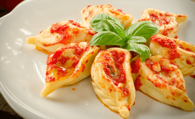 Ravioli cotti con salsa rossa su un piatto bianco, guarniti con una sprigiona di basilico fresco al centro.