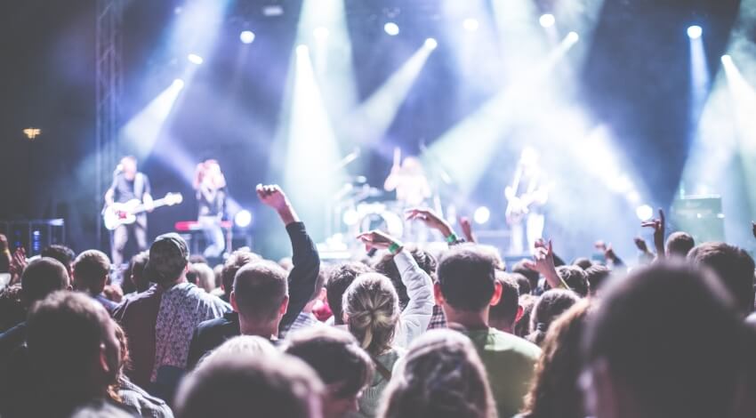 Una folla entusiasta a un concerto, con persone che alzano le braccia e quattro musicisti sul palco che suonano.