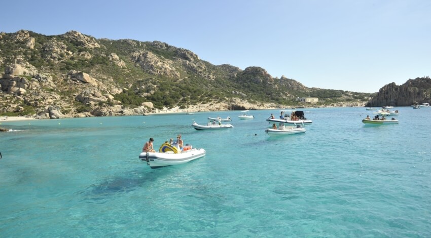 Barche in acqua turchese con colline rocciose e vegetazione sullo sfondo.