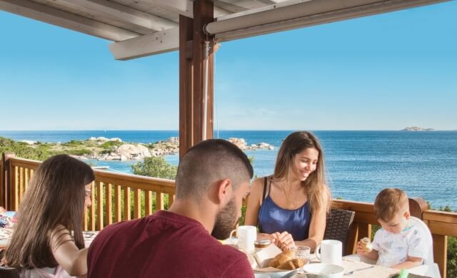 Une famille de quatre personnes dîne sur une terrasse surplombant l'océan par une journée ensoleillée.