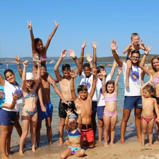 Un gruppo di 17 persone, tra cui bambini e adulti, posa sulla spiaggia con il mare sullo sfondo.