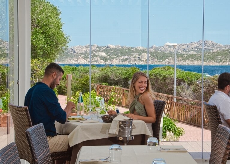 Una coppia cena in un ristorante vista mare, con pane e oggetti sul tavolo tra loro.