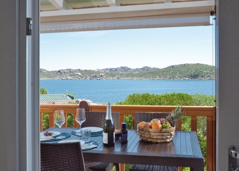Dining table set with fruit, wine, and scenic water view.