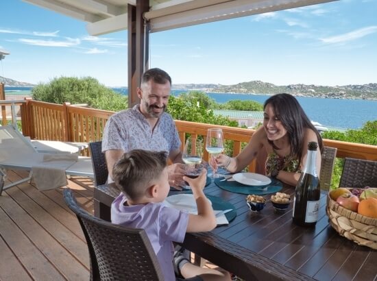 Familie sitzt an einem eleganten Tisch im Freien, umgeben von Natur, mit Wein und Snacks, in einer entspannten Atmosphäre.