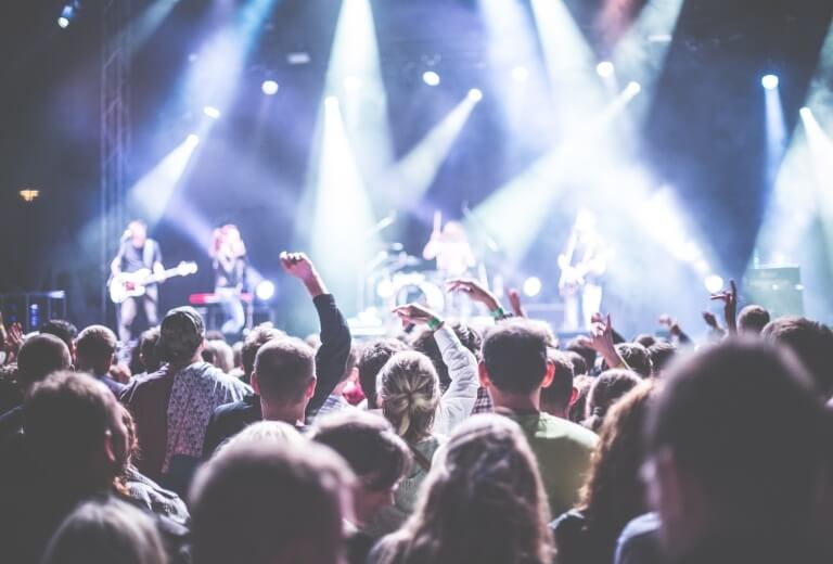 Ein lebhaftes Konzert mit einer begeisterten Menge vor einer beleuchteten Bühne, wo eine Band auftritt.