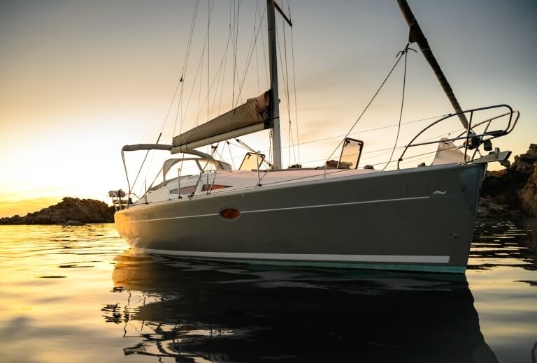 Segelboot im ruhigen Wasser, bei Sonnenuntergang, mit weißem Rumpf und grauem Rumpf, nicht im Einsatz.
