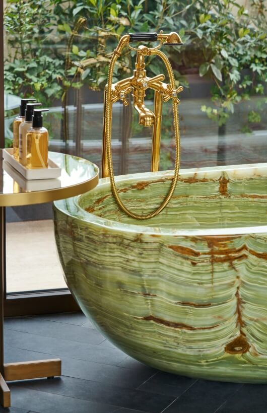 Luxurious bathroom with a green marble bathtub, gold fixtures, black floor, and a side table with soap bottles.