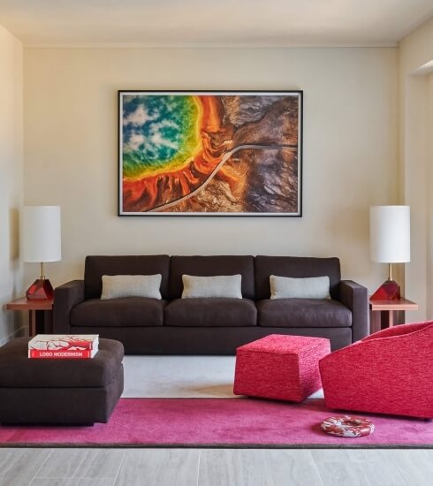Living room with a brown couch, pink rug, vibrant abstract painting, and red lamps on end tables, creating a stylish ambiance.