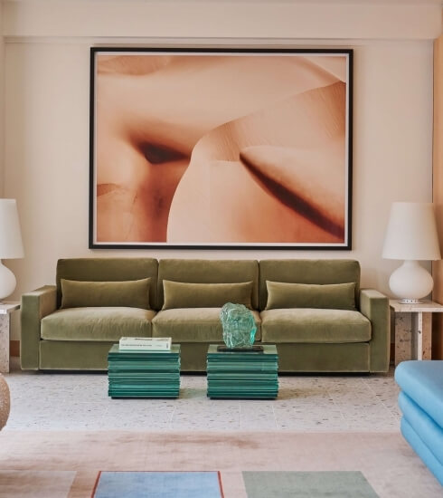 Cozy living room with a green couch, abstract art, glass sculptures, white lamps, and a blue-green rug, exuding relaxation.