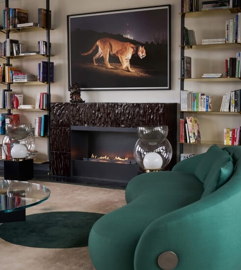 Luxurious living room with a fireplace, bookshelves, green couch, and elegant decor, featuring a lion painting above the fireplace.