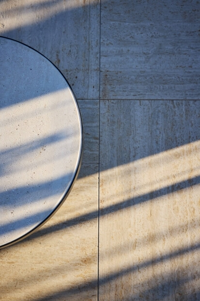 Close-up of a round white tabletop with dark speckles on a beige tiled floor, featuring soft lighting and gentle shadows.