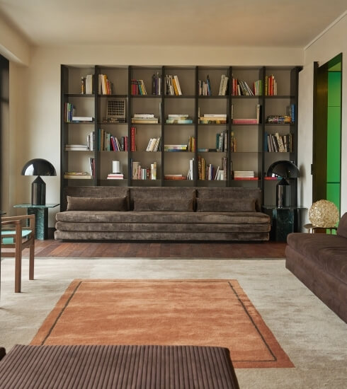 Spacious living room with gray sofa, brown armchairs, wooden bookcase, and elegant decor, featuring warm lighting and a cozy rug.