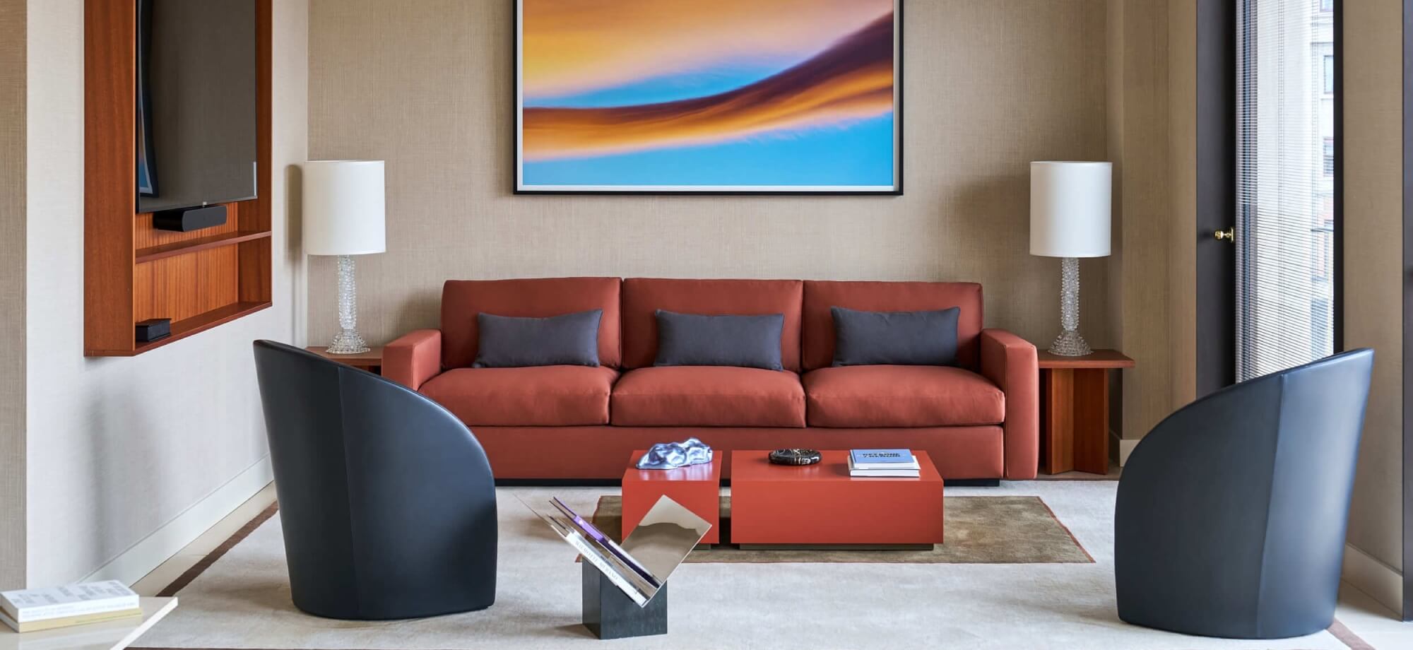 Modern living room with salmon couch, black chairs, abstract painting, and natural light, exuding comfort and sophistication.