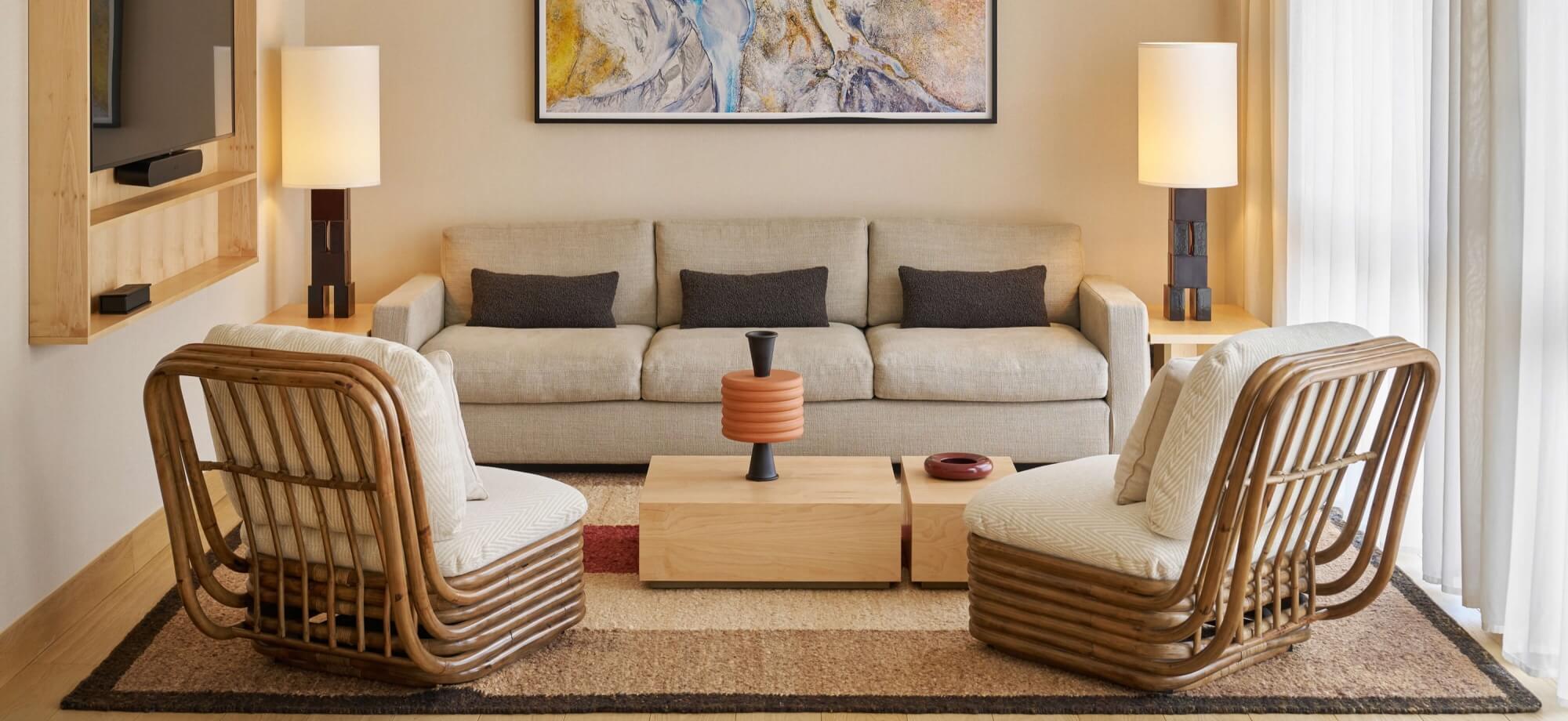 Cozy living room with a light sofa, wooden chairs, coffee table, and abstract painting, featuring a neutral color scheme.