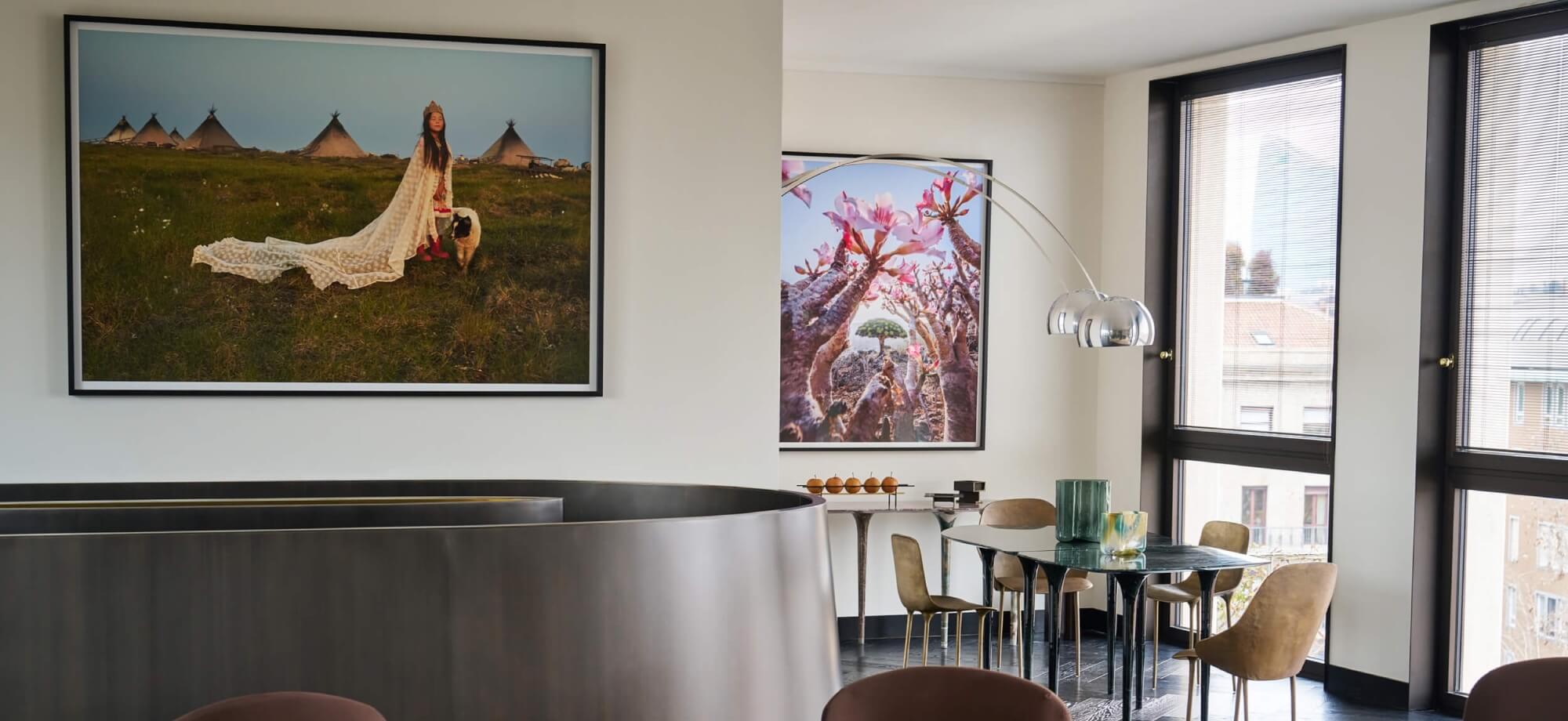 Modern dining room with a black table, tan chairs, framed photographs, and a window showing buildings outside.