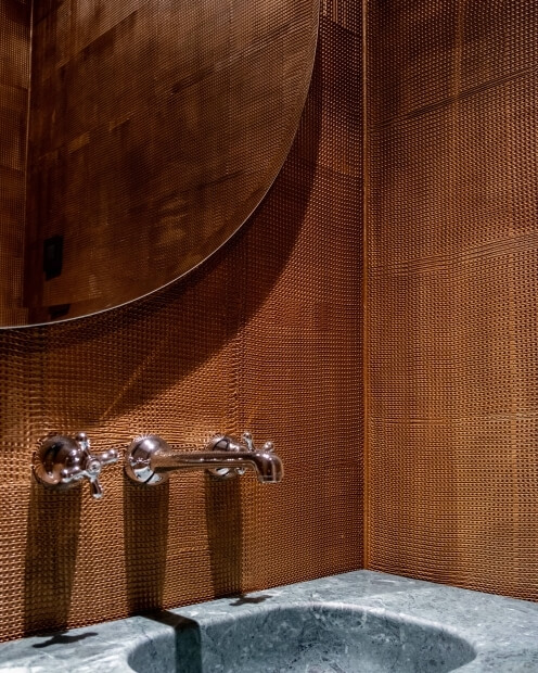 Modern bathroom sink with gray marble countertop, metal faucet, round mirror, and warm brown wall tiles.