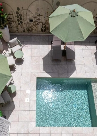 Vista dall'alto di un patio con piscina, ombrelloni verdi e arredi, trasmette un'atmosfera di relax e lusso.