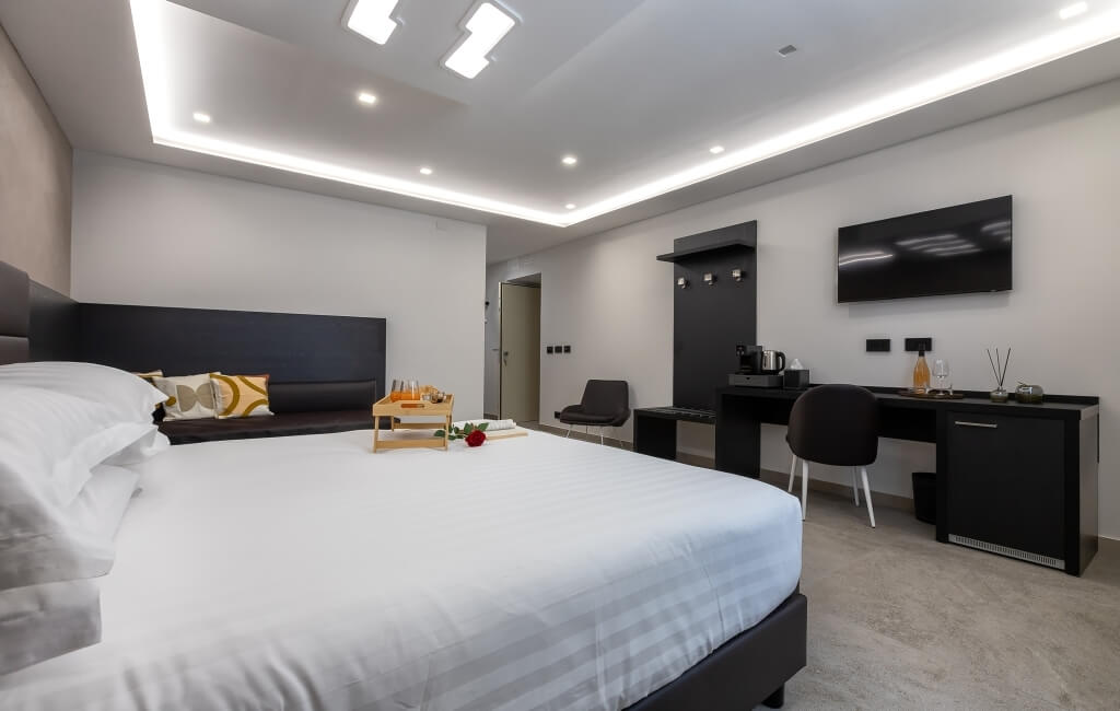 Camera d'hotel moderna con letto grande, area scrivania, TV a parete e accessori come caffettiera e frigorifero.