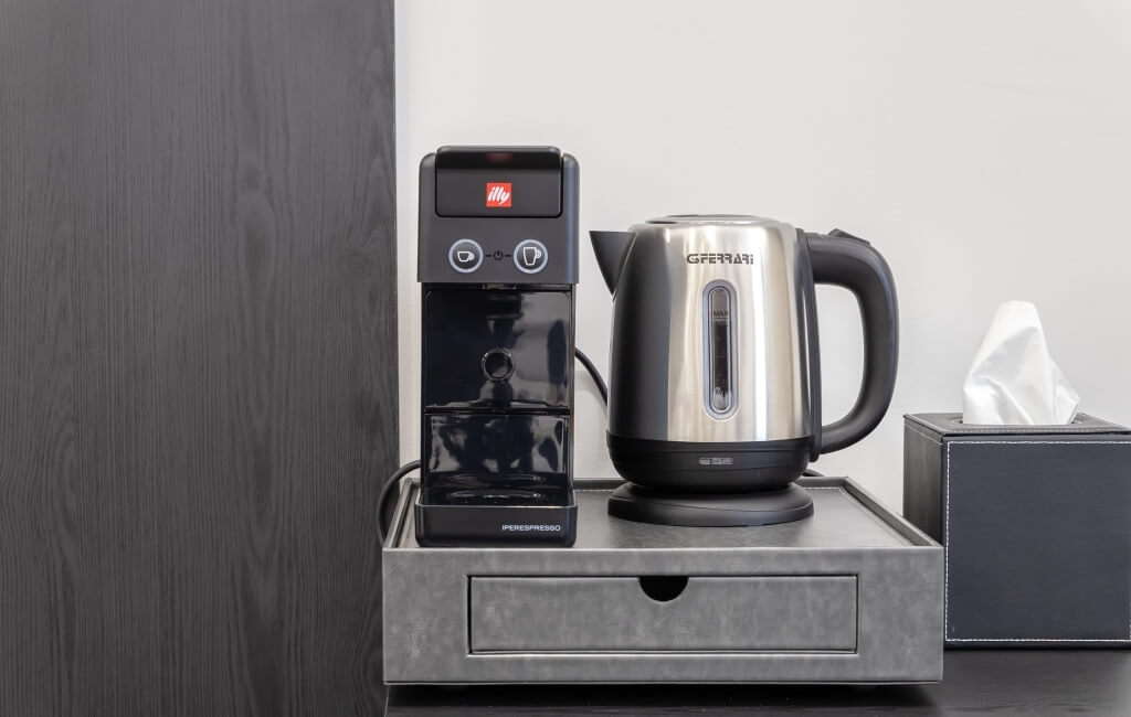 Contatore cucina con macchina da caffè, kettle elettrico e scatola di fazzoletti su un vassoio metallico.