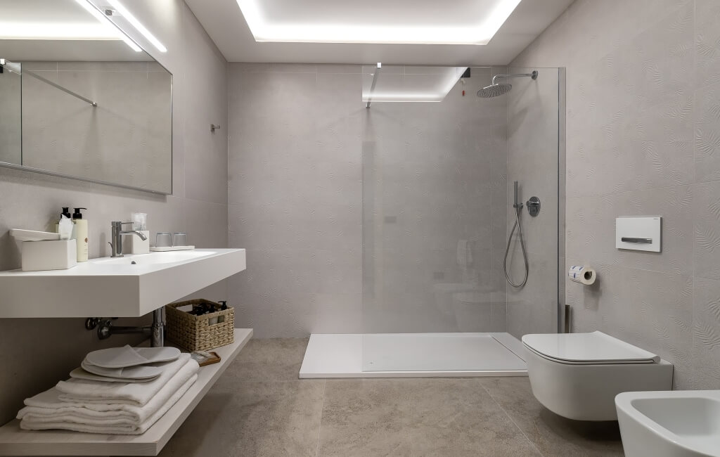 Bagno moderno e minimalista con specchio grande, lavabo bianco, doccia in vetro e illuminazione calda.