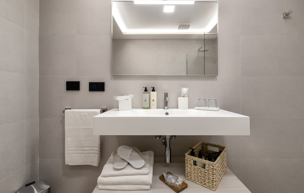 Bagno moderno con lavabo bianco, specchio grande, asciugamani bianchi e doccia con soffione in acciaio.