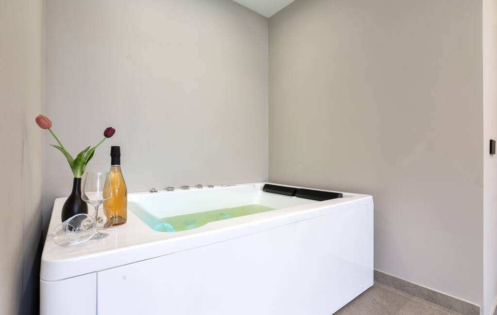 Bagno sereno con vasca bianca, tulipani, vino e bicchieri, pareti grigie e pavimento chiaro. Atmosfera rilassante.