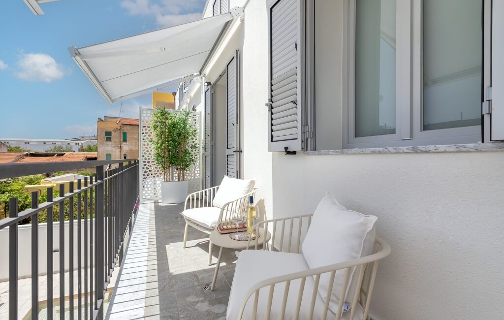 Balcone sereno con due sedie bianche, un tavolo con vino e bicchieri, e una pianta in un ambiente invitante.