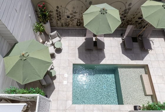 Vista aerea di una piscina rettangolare con vasca idromassaggio, ombrelloni verdi e atmosfera rilassante.