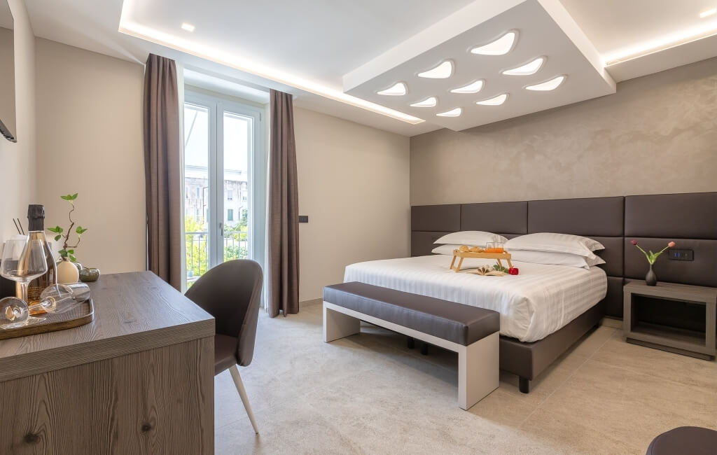 Camera d'albergo moderna con letto, scrivania e finestra luminosa. Decorazioni eleganti e colori chiari.