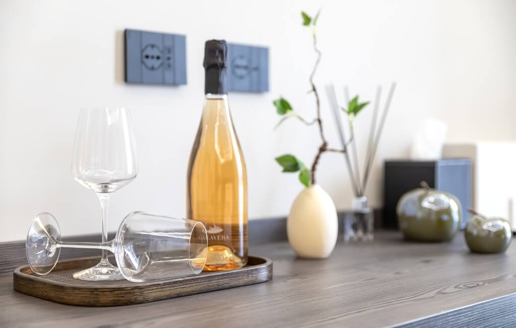 Una bottiglia di vino rosato su un vassoio di legno con due bicchieri vuoti, uno in posizione verticale e l'altro sdraiato.