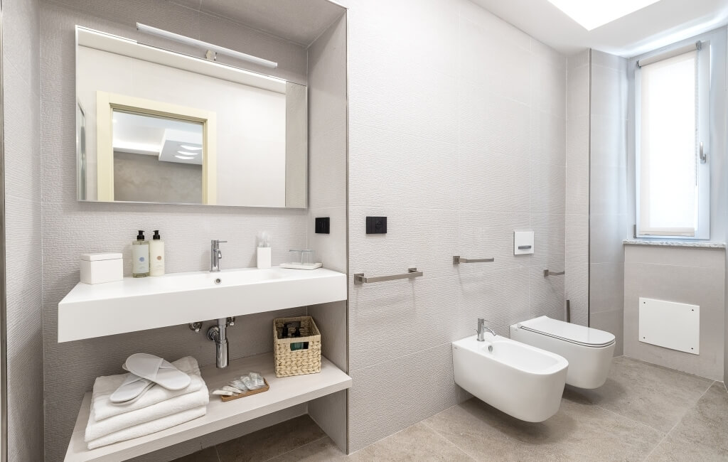 Bagno moderno minimalista bianco e grigio con specchio grande, lavabo, asciugamani bianchi e bidet. Luce naturale.