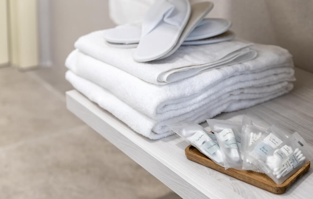 Tovaglioli bianchi piegati su un vassoio di legno, con ciabatte bianche sopra, su uno scaffale di un bagno.