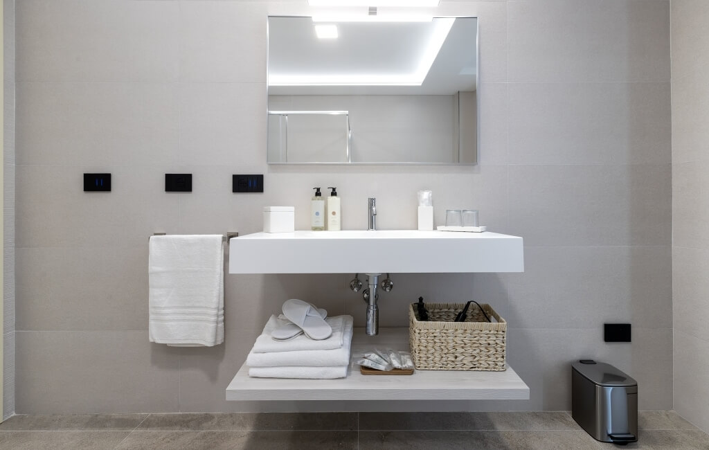 Bagno moderno con lavabo bianco a muro, mensola galleggiante, asciugamani piegati e accessori per la cura personale.