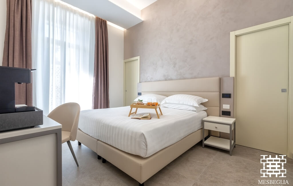 Camera d'hotel moderna e serena con letto beige, biancheria bianca, tavolino e luci, decorata in toni neutri.