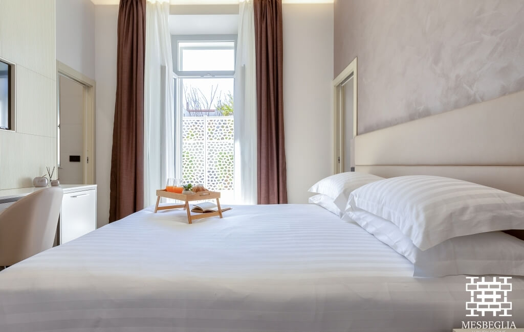 Camera d'hotel serena con letto centrale, decor minimalista, luce naturale e vista su una parete decorativa.