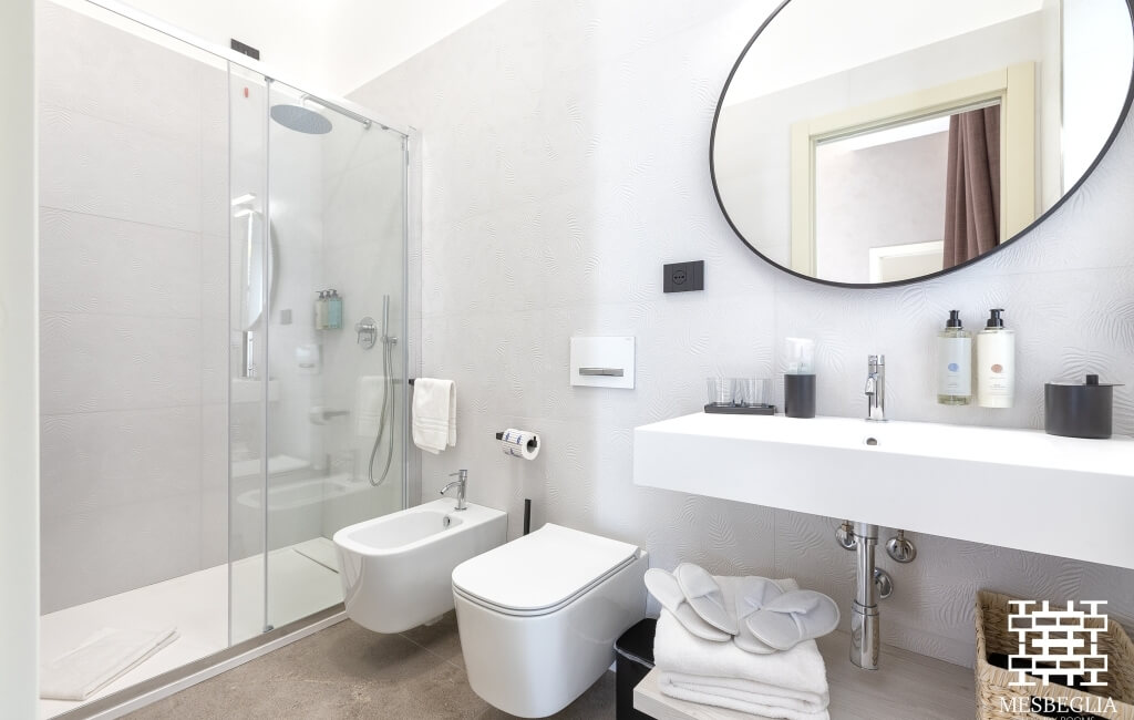 Bagno moderno minimalista con doccia in vetro, WC a parete e lavabo galleggiante, decorato con asciugamani bianchi.