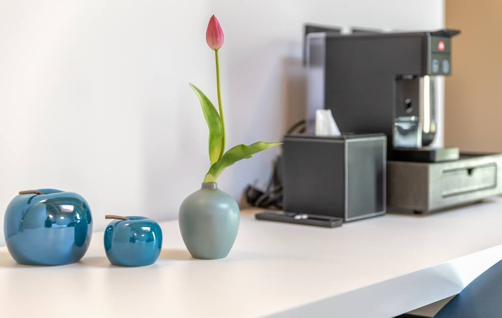 Spazio di lavoro sereno con vasi blu, un tulipano rosa e una macchina da caffè nera su un piano bianco.